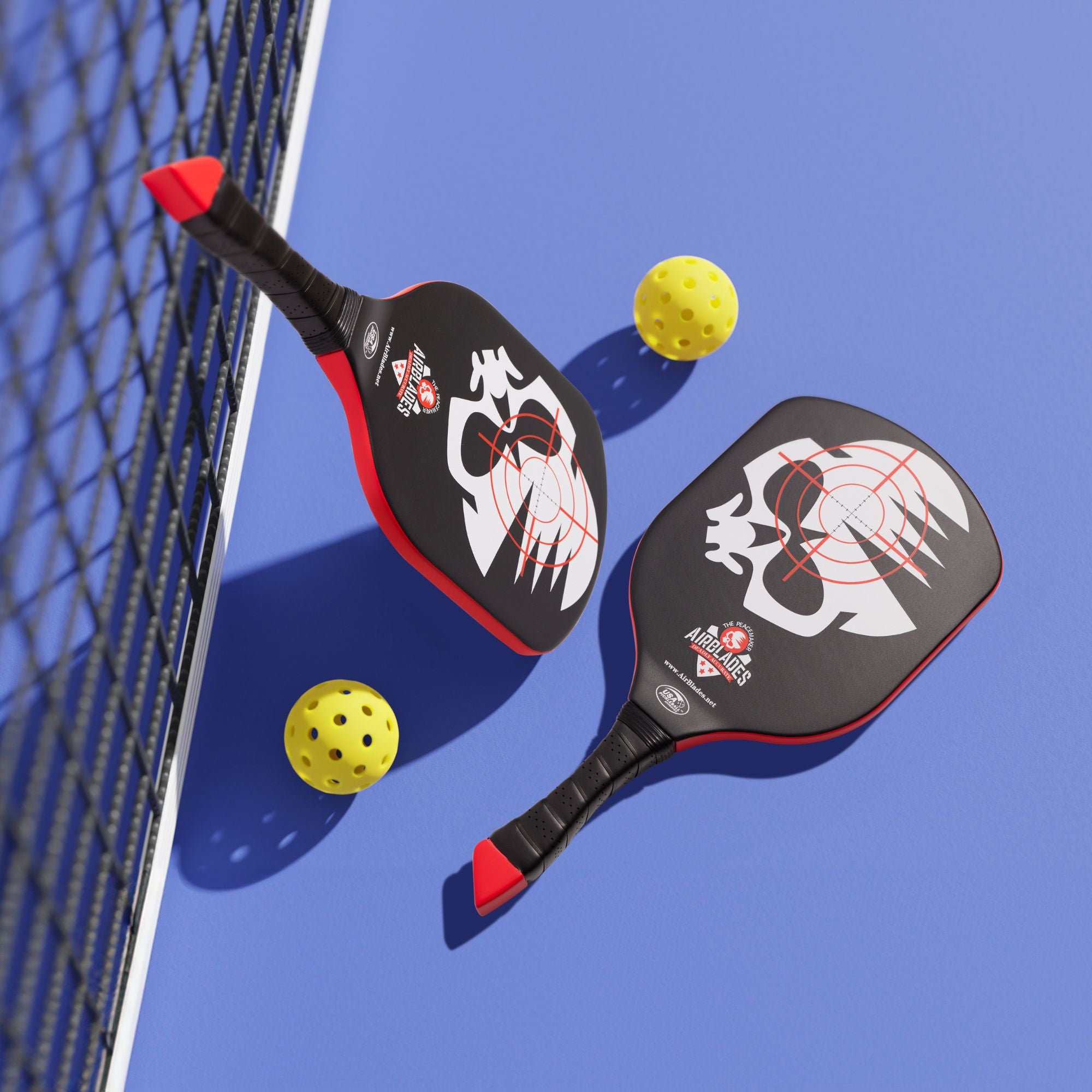 Two Australian-designed AirBlades Peacemaker Pickleball Paddles with patented SlopeHandle grip on a blue court beside yellow pickleballs.