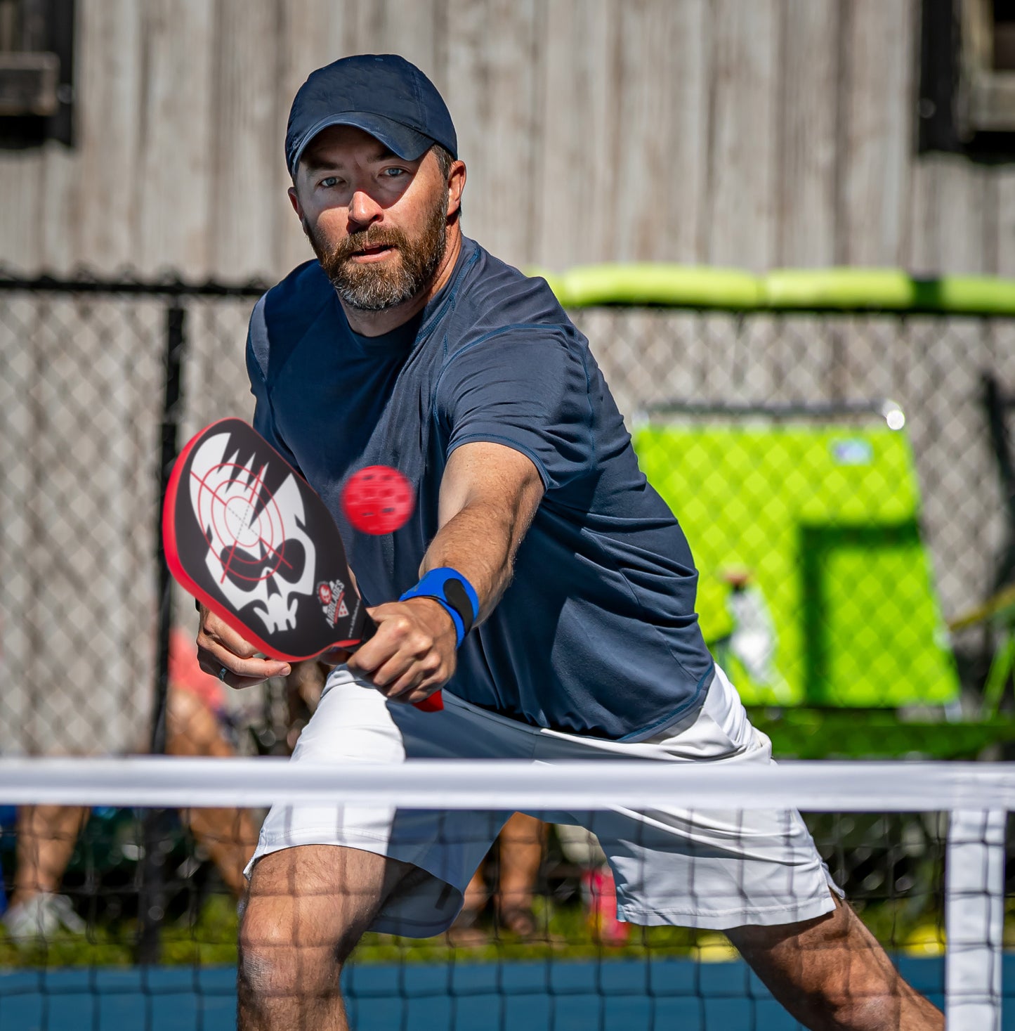 Man playing pickleball outdoors using the AirBlades Peacemaker Pickleball Paddle with patented SlopeHandle grip, striking a red ball at the net.